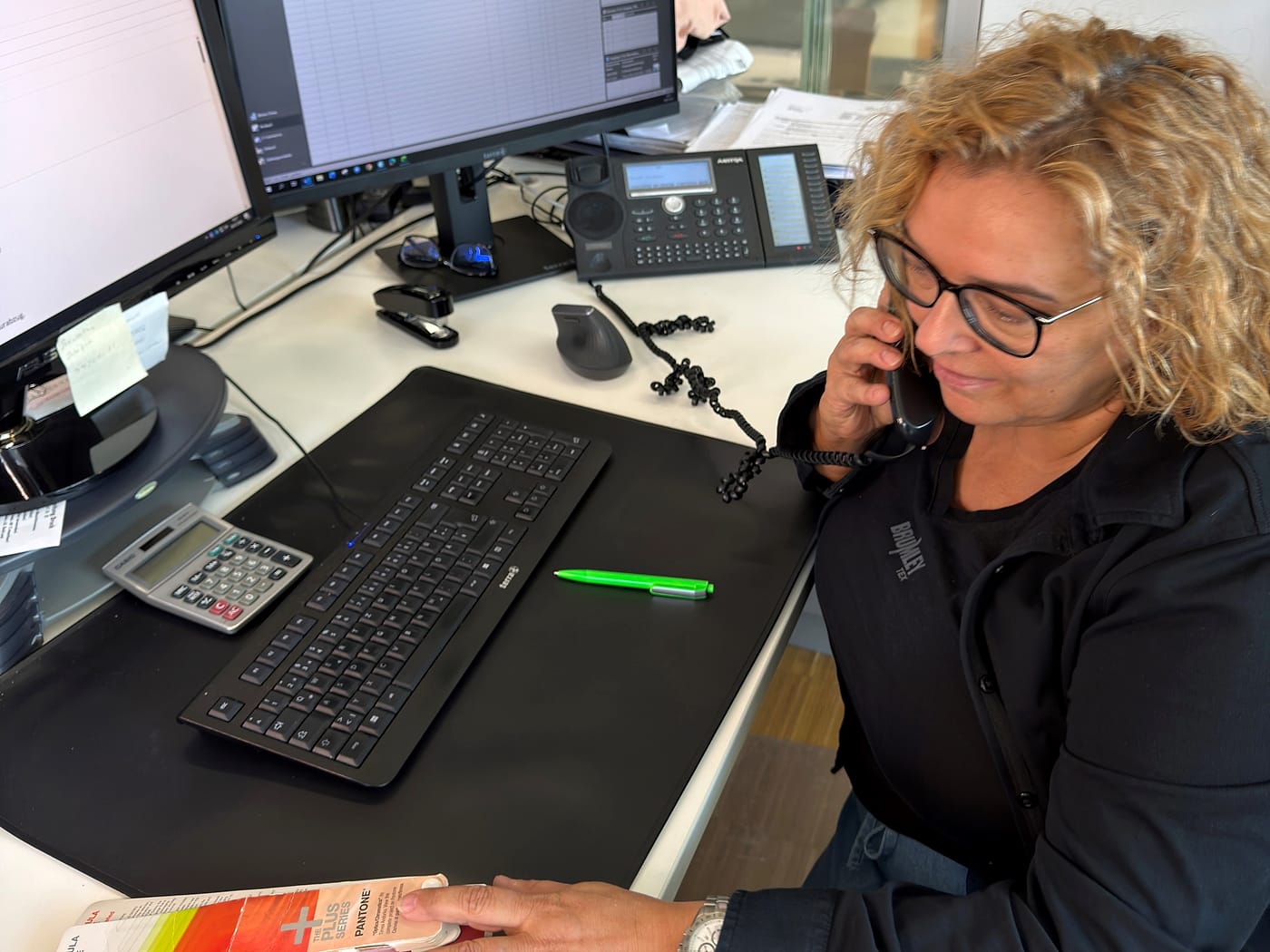 Britta Schneider telefoniert an ihrem Arbeitsplatz bei JobOutfit, neben Tastatur und Farbfächer