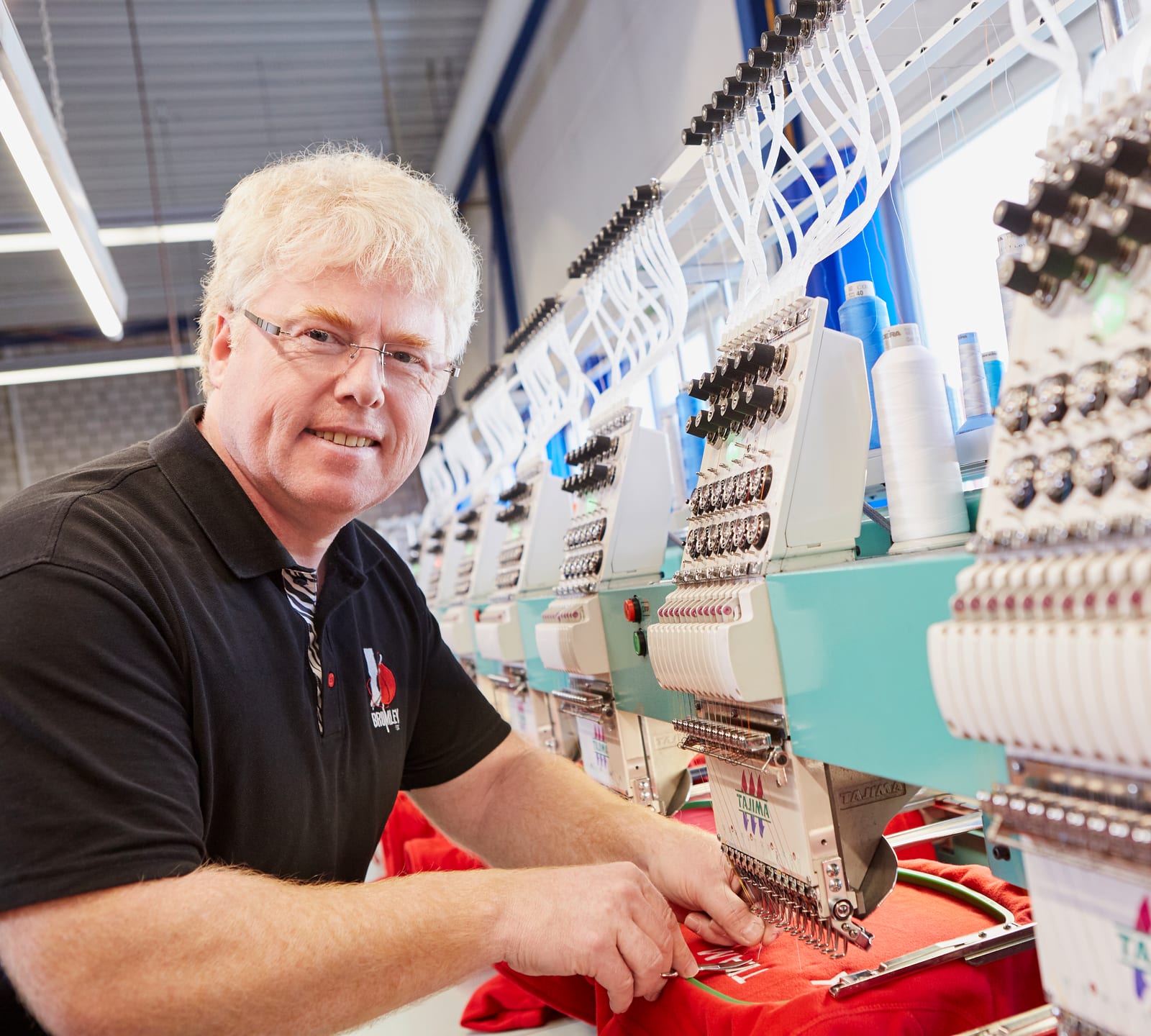 Mitarbeiter richtet an einer Mehrkopf-Stickmaschine ein rotes Shirt ein