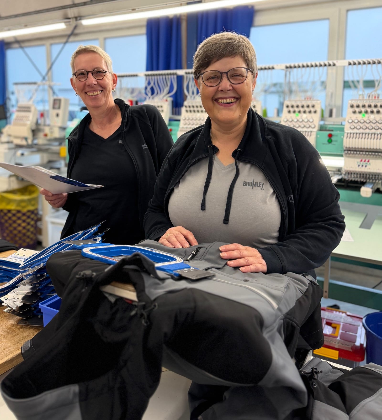 Zwei Mitarbeiterinnen richten Arbeitsjacken an den Stickmaschinen in der JobOutfit-Produktion in Emsdetten ein