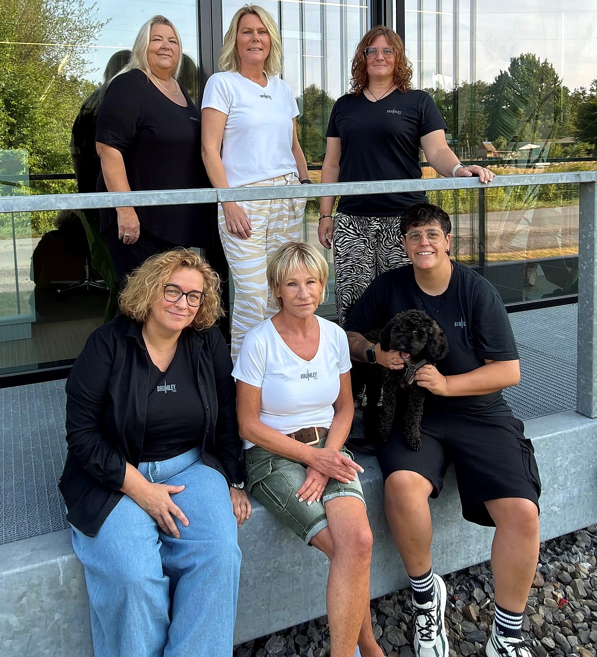 Sechs Mitarbeiterinnen von JobOutfit stehen und sitzen vor dem Firmengebäude in Emsdetten