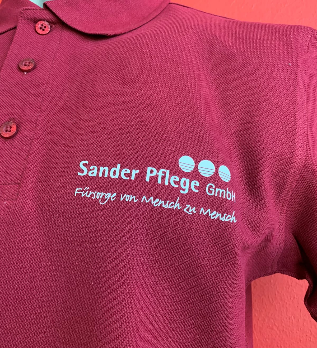 Bedrucktes weinrotes Poloshirt mit hellblauem Firmenlogo eines Pflegedienstes